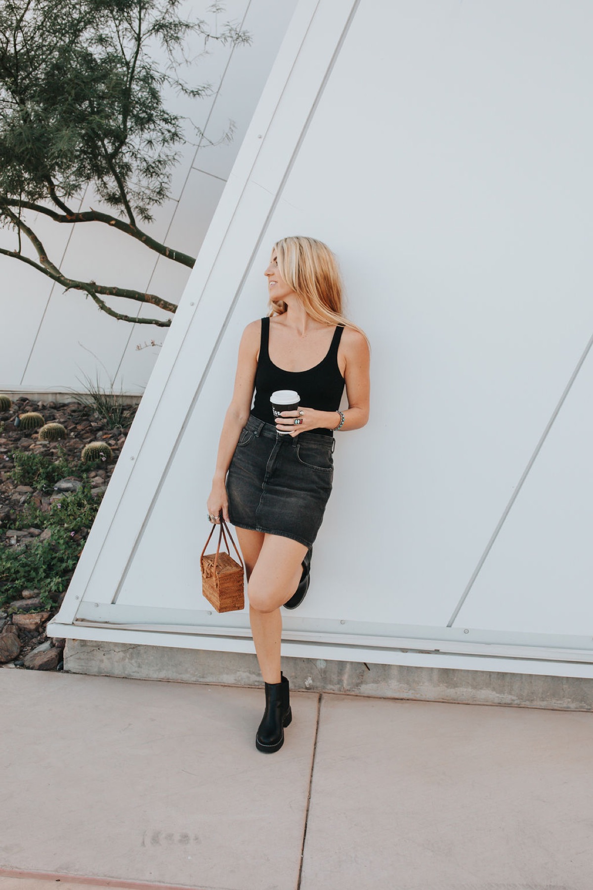 Dakota Jeane leaning against a white wall holding a coffee